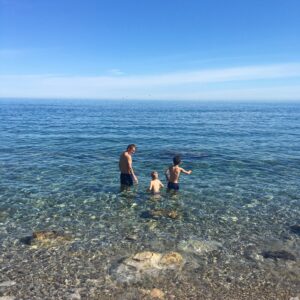 Rodina si užívá jarního koupání v průzračném moři na písečné pláži Sardinie